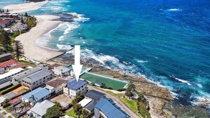 An aerial view of a coastal residential area with houses, a beach, and a rocky shoreline. - Beachfront Penthouse at The Entrance - Beach Pool right infront (The Entrance)