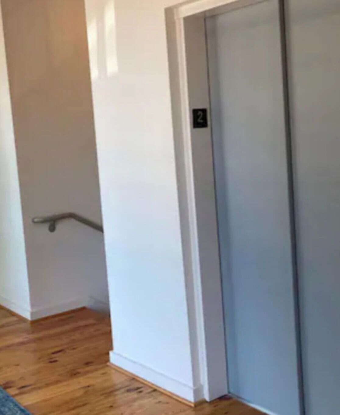 A hallway with a white door, a handrail, and wooden flooring.