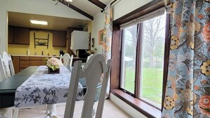 Een eetruimte met een tafel voor vier personen, een raam met bloemen gordijnen, en uitzicht op een gazon.