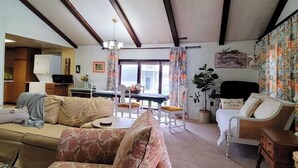 Een woonkamer met een bank, een eettafel met stoelen, een open haard en een groot raam.