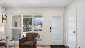 Una sala de estar con un sillón estampado, un sofá gris, una mesita con una lámpara y vistas al exterior a través de un ventanal.