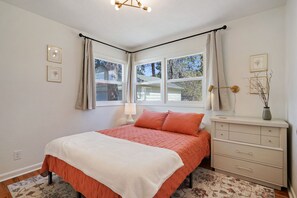 A bedroom with a bed, a dresser, a window with curtains, and a lamp.