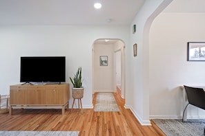A modern living room with a wooden cabinet, a flat-screen TV, a potted plant, and a hallway leading to another room.