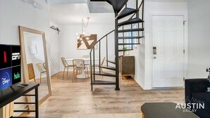 Un intérieur moderne avec un escalier en colimaçon, un coin repas et un téléviseur permettant d’accéder aux services de diffusion en continu.