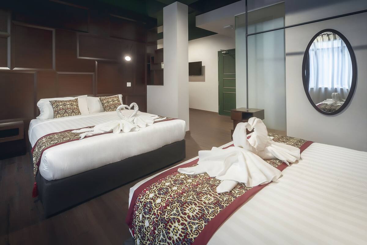 A hotel room with two beds, a large mirror, and a television on the wall.