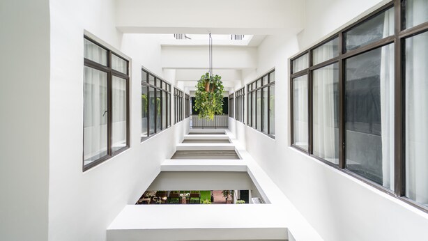 Un interior moderno con una escalera central, ventanas amplias y una planta colgante.