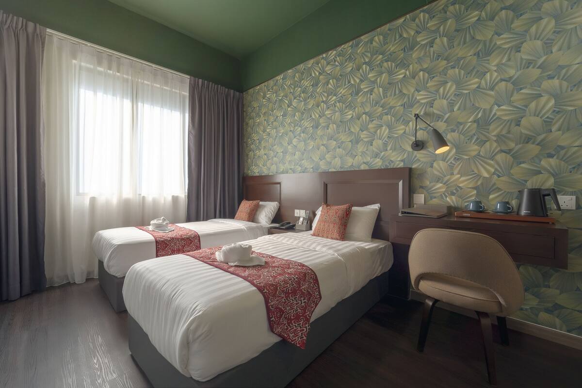 A hotel room with two beds, a desk, a chair, and a window with curtains.