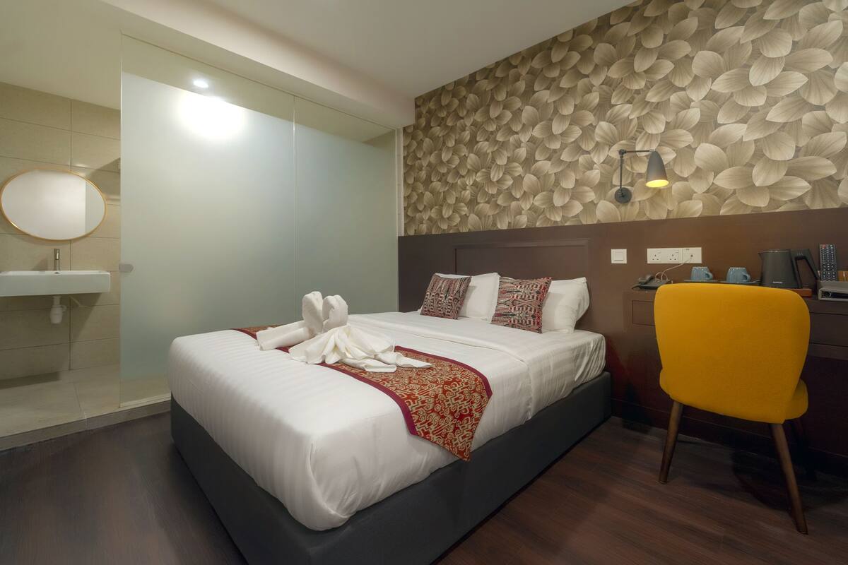 A hotel room with a bed, a desk, a chair, a mirror, and a wall with a leaf pattern.