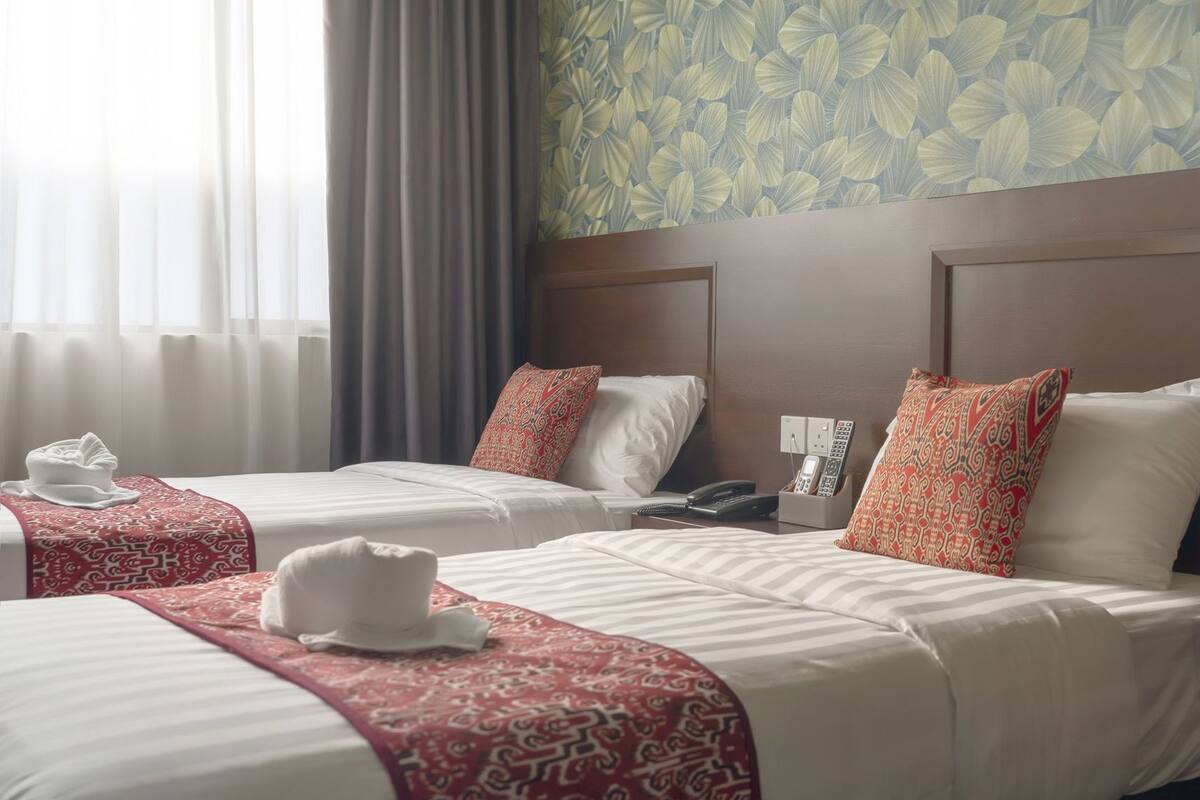 A hotel room with two beds, a telephone, and a wall with a floral pattern.