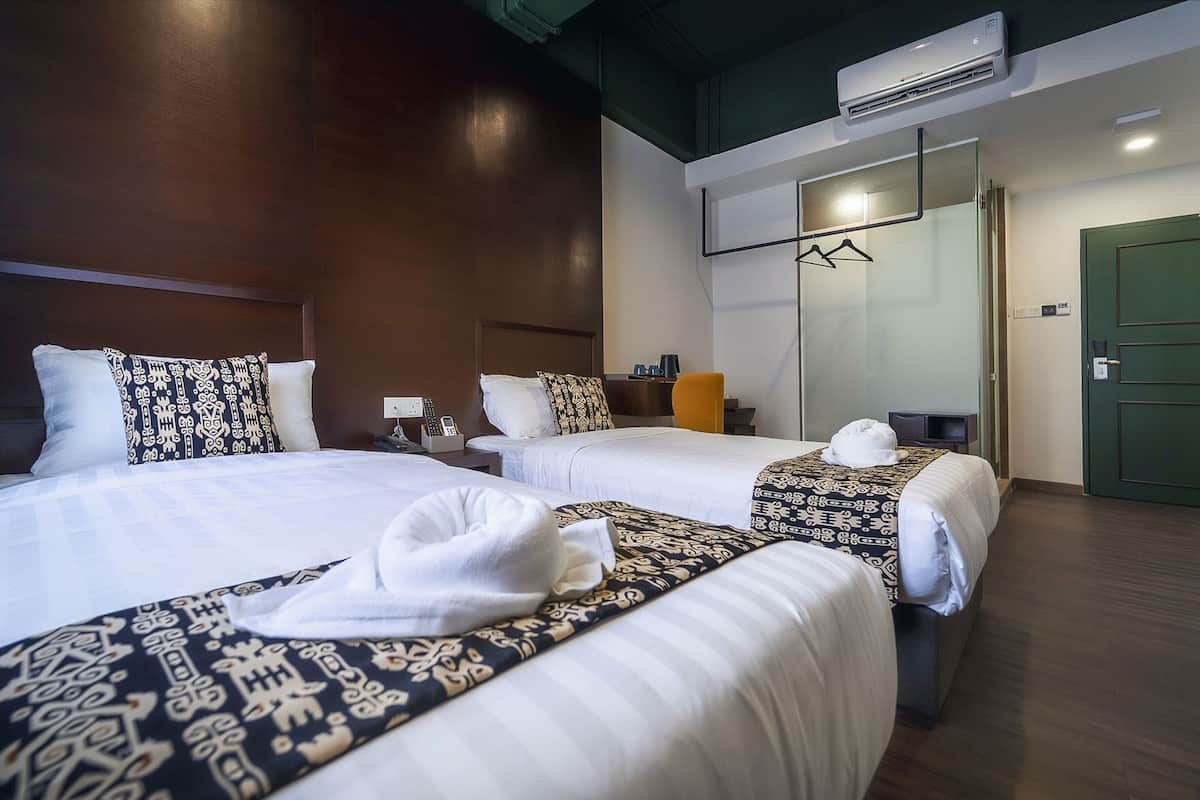A hotel room with three beds, a desk, a chair, an air conditioning unit, and a green door.