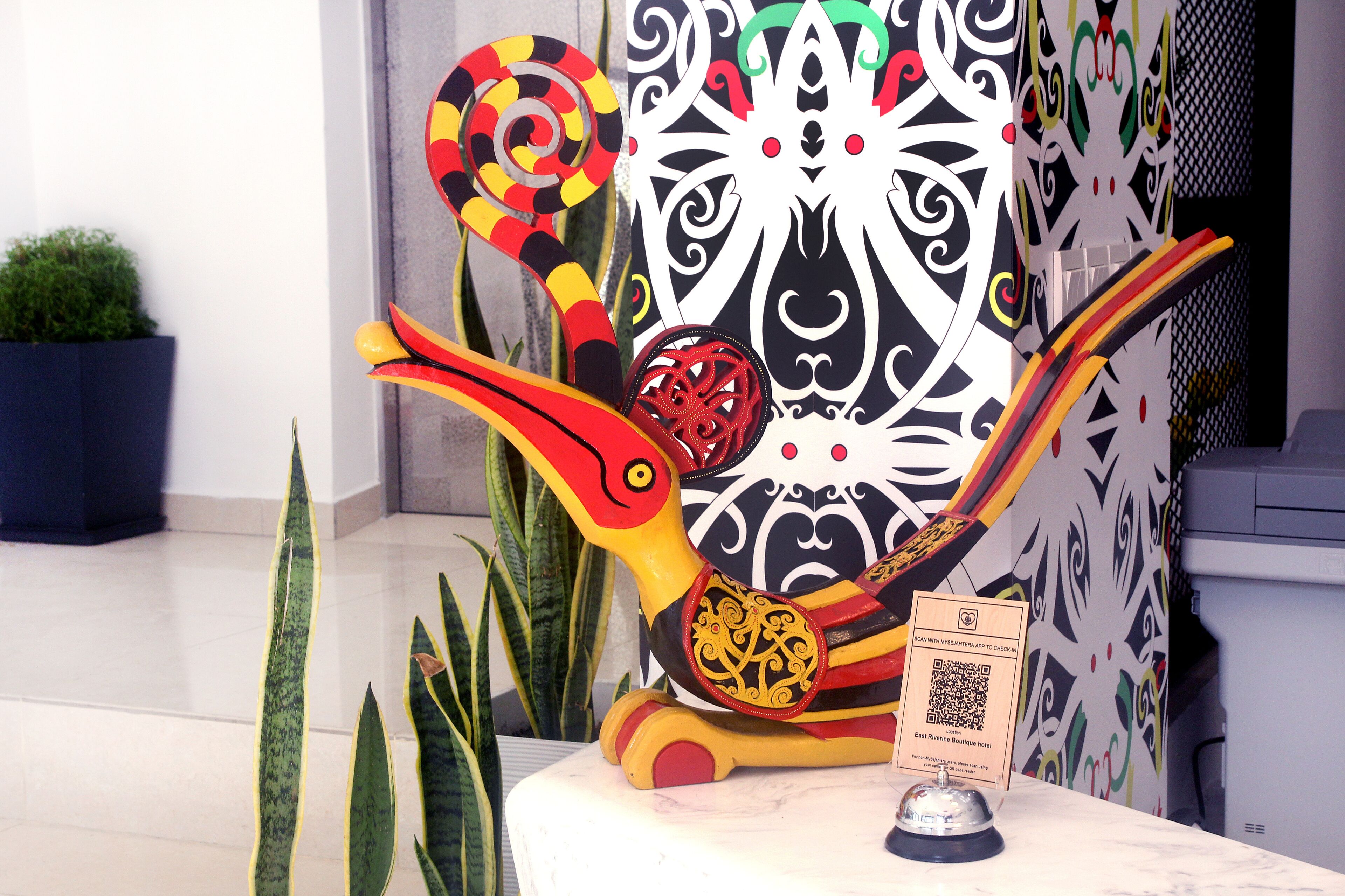 Eine dekorative Vogel-Skulptur mit rot-gelbem Körper, platziert auf einer weißen Oberfläche.