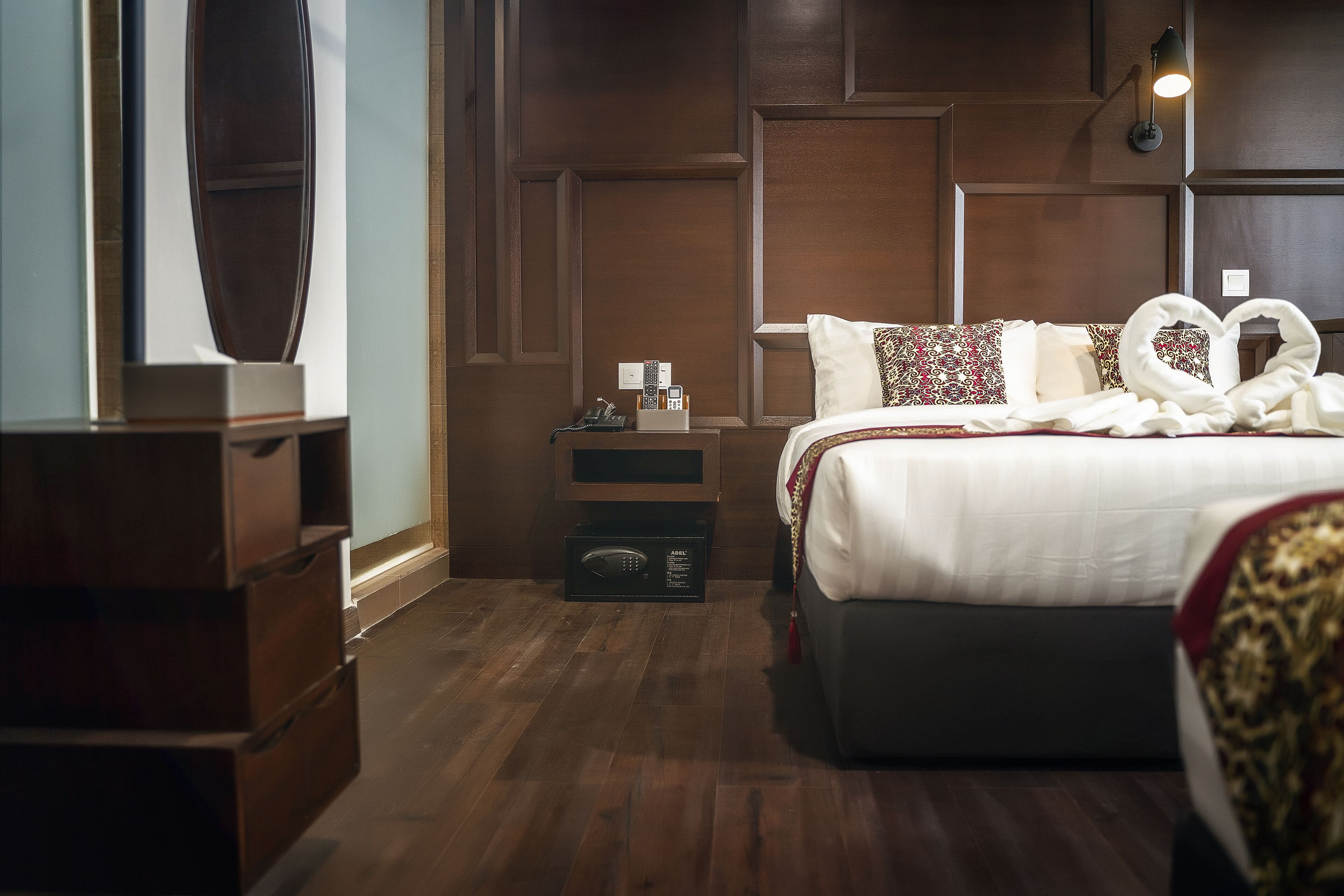 A hotel room with a large bed, a bedside table with a lamp, and a wooden dresser.