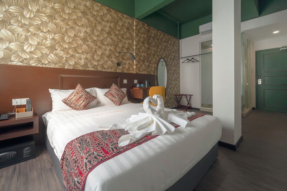 Quarto de hotel com uma cama grande, mesa de cabeceira com telefone e carregador, espelho e guarda-roupa.