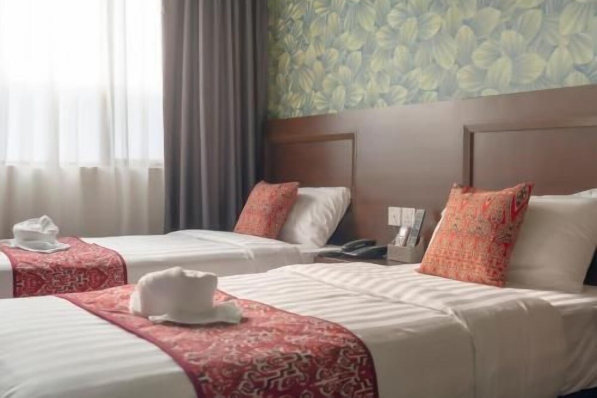Quarto de hotel com duas camas, cabeceira, telefone e janela com cortinas.