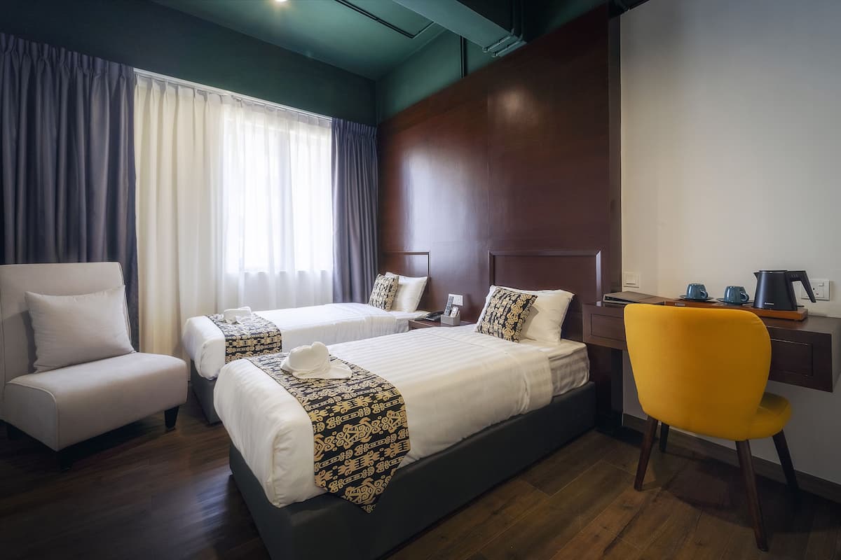 A hotel room with two beds, a desk, a chair, and a large window with curtains.