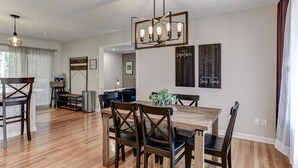 A dining area with a wooden table and chairs, a hanging light fixture, and a wall with a framed artwork. - Updated home, hot tub, fire pit close to Asheville (Candler)