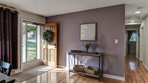 A room with a sliding glass door leading to a garden, a console table with baskets, and a framed inspirational quote on the wall. - Updated home, hot tub, fire pit close to Asheville (Candler)