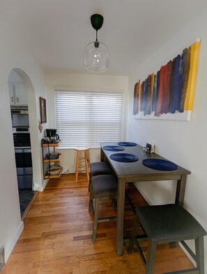 Een eetruimte met een houten tafel, blauwe placemats en een moderne hanglamp.