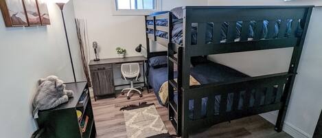 A dormitory room with bunk beds, a desk, a chair, a lamp, a plant, and a window.