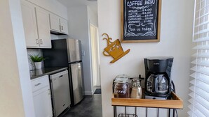 Cozinha com armários brancos, uma máquina de café e um menu em lousa.