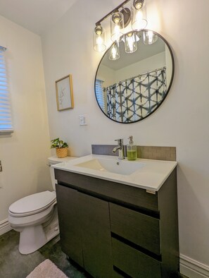 Een badkamer met een wit toilet, een wastafel met een spiegel erboven en een douchegordijn met een geometrisch patroon.
