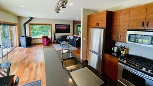 A modern kitchen with wooden cabinets, stainless steel appliances, and a dining area with a red chair and a black sofa.