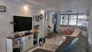 Un salon comprenant un grand téléviseur à écran plat, un canapé, une table basse et un coin repas avec des chaises.