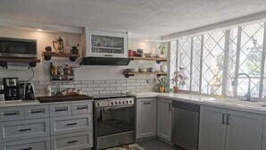 Une cuisine moderne avec des meubles blancs, un four encastré et un lave-vaisselle. Des étagères au-dessus du plan de travail servent à ranger divers ustensiles de cuisine.