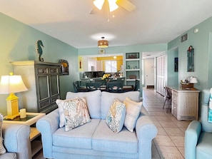 A living room with a sofa, a dining table, and a kitchen in the background.
