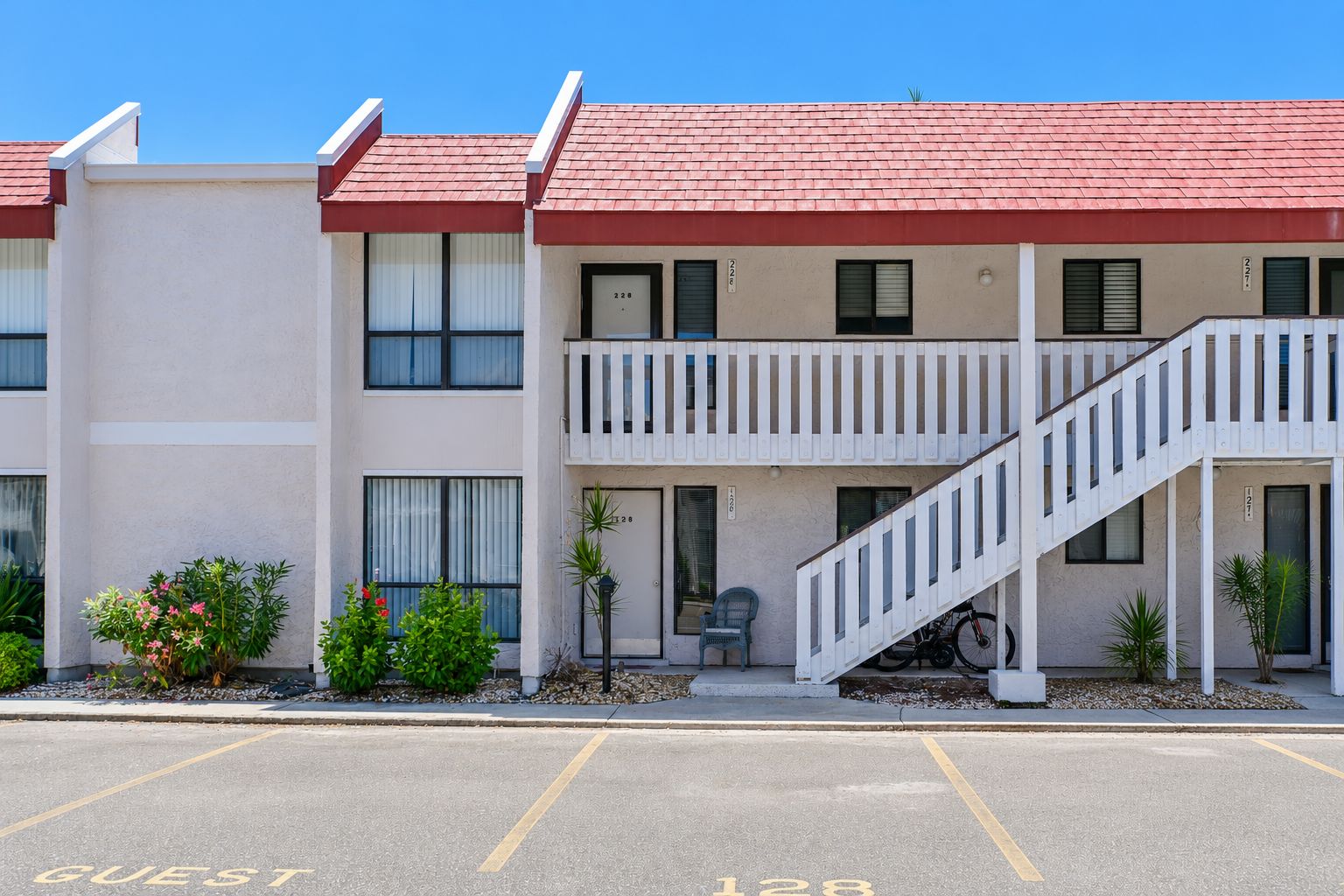 Un motel de dos pisos con techo rojo, un balcón en el segundo piso y un estacionamiento que indica 'GUEST 128'.