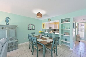 A dining area with a wooden table and chairs, a kitchen in the background, and a teal color scheme. - Runaway Bay 128 - Beach, Pool, gym and bay (Bradenton Beach)