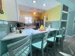 A kitchen with a central island, chairs, a refrigerator, and a window.