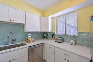 A kitchen with white cabinets, a dishwasher, a toaster, and a blender on the counter.
