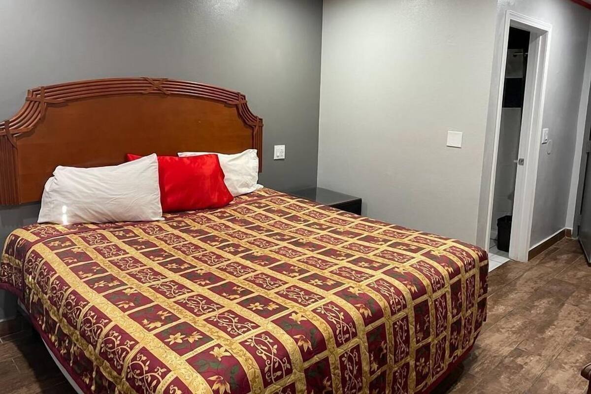 A bedroom with a large bed, a wooden headboard, and a red and gold patterned bedspread.