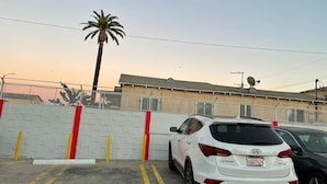 A white SUV parked in a parking lot with a white wall and red and yellow bollards. - The Broadway Inn (Los Angeles)