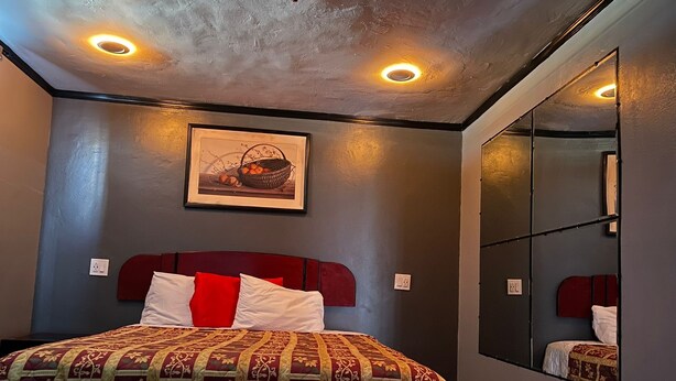 A bedroom with a bed, a headboard, a wall-mounted mirror, and a framed picture. - The Broadway Inn (Los Angeles)