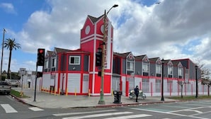 A motel with a distinctive red and white facade, a prominent tower, and a crosswalk at the intersection. - The Broadway Inn (Los Angeles)