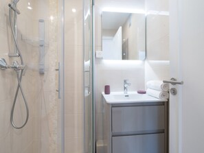 Une salle de bain moderne avec une douche à parois de verre, un lavabo blanc et un miroir au-dessus.