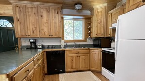 Una cocina con armarios de madera, lavavajillas, refrigerador, microondas y una ventana con vista a árboles.
