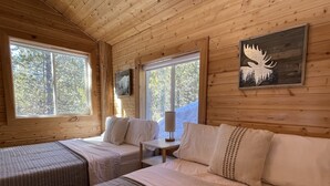 Una cabaña con dos camas, una mesita y una lámpara. Se ven ventanas con vistas a árboles.