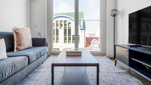 Uma sala de estar moderna com sofá, mesa de centro, televisão e uma grande janela com vista para edifícios.