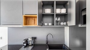 Uma cozinha moderna com armários cinza, forno embutido, pia e prateleira de madeira acima do forno.