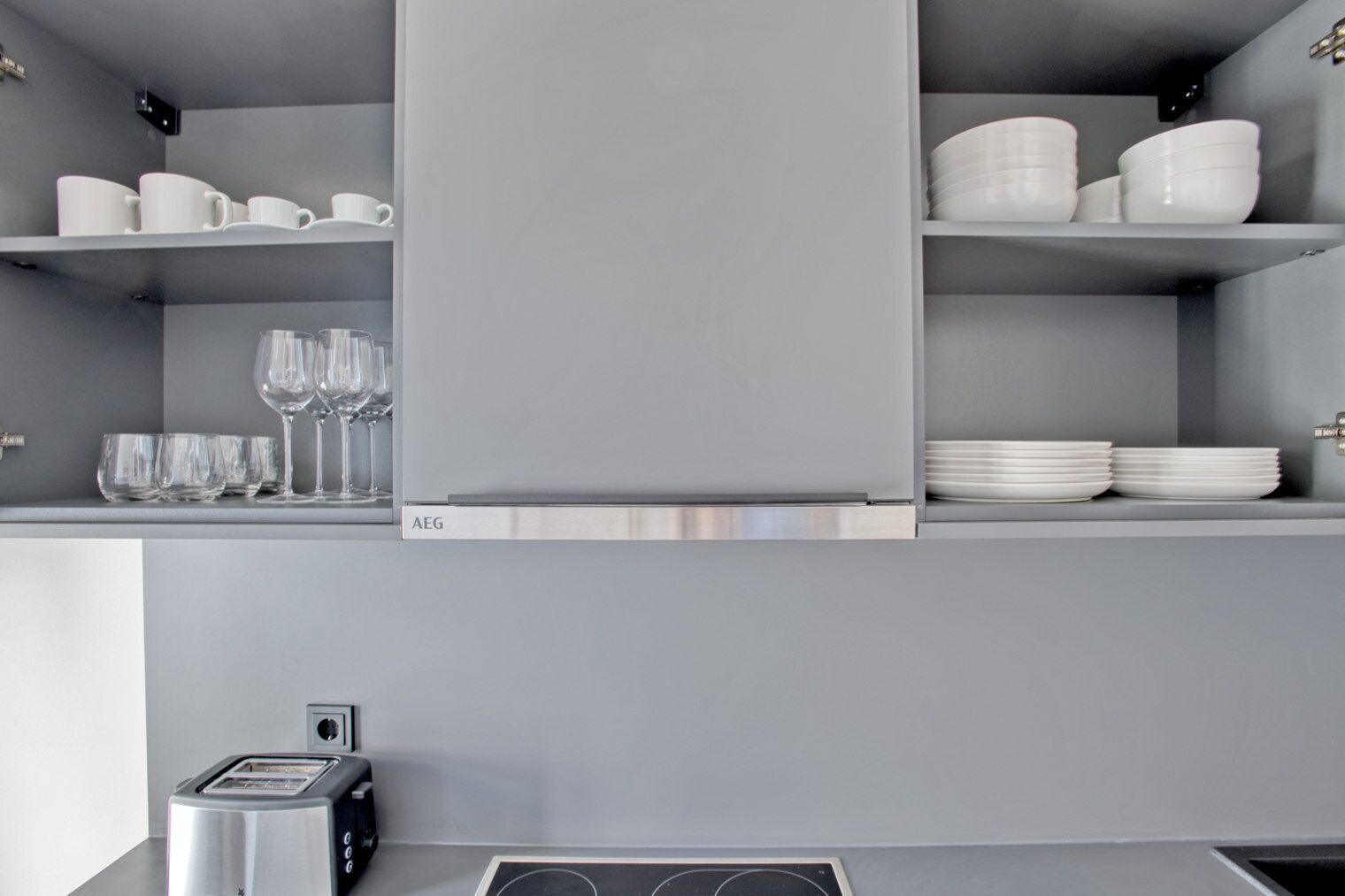 A modern kitchen with grey cabinets, a stainless steel range hood, and a built-in toaster.