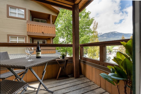 A balcony with a table, chairs, a bottle of wine, and a potted plant.