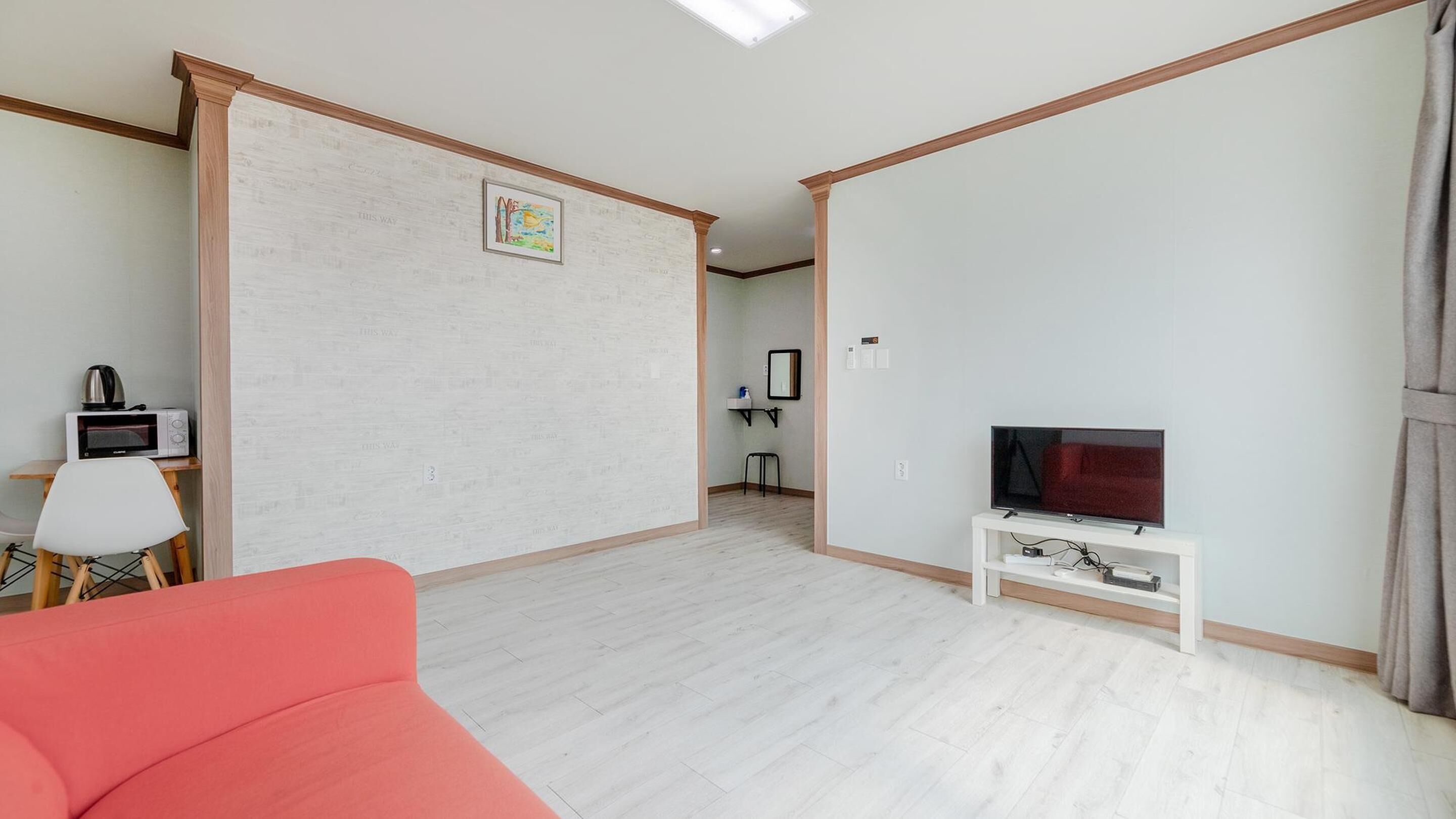A modern living room with a flat-screen TV, a red sofa, a microwave, and a small table.
