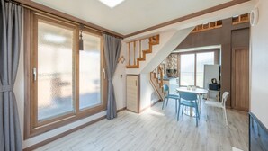 Una habitación amplia con un gran ventanal corredero, una escalera que sube a un nivel superior y una pequeña zona de comedor con sillas azules.