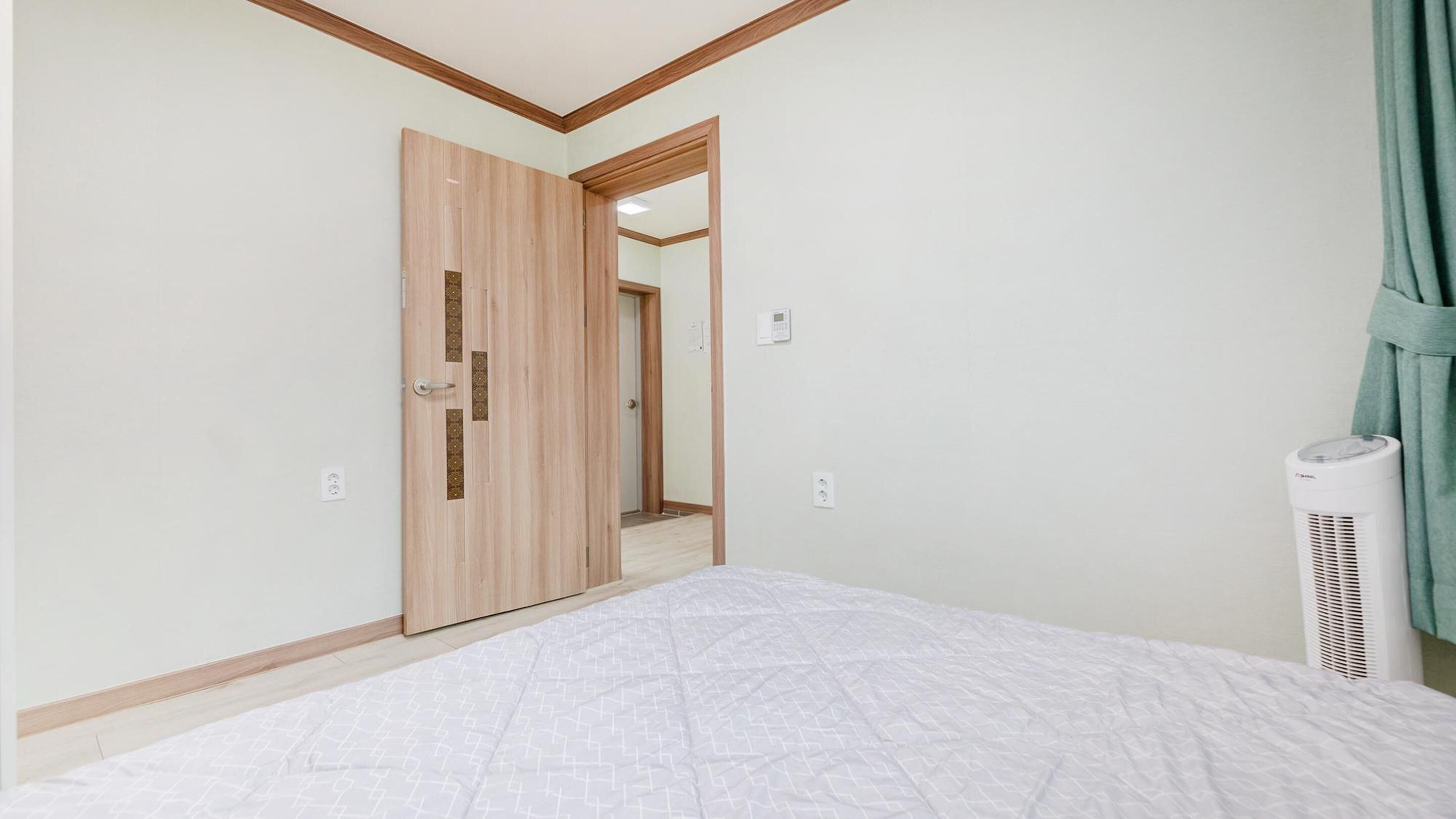 Een slaapkamer met een bed, een houten kledingkast, een deur, een wandairconditioner en een lichtschakelaar.