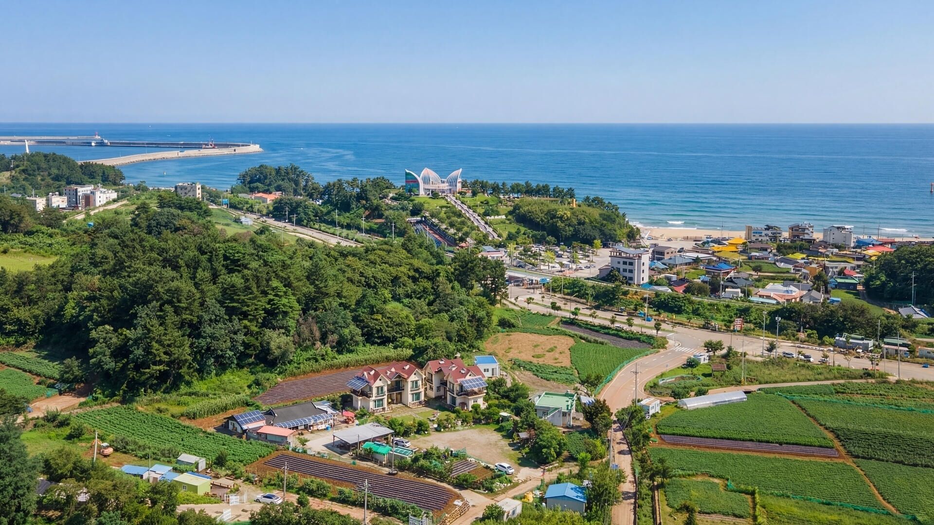 An aerial view of a coastal town with residential buildings, a lighthouse, and a beach.