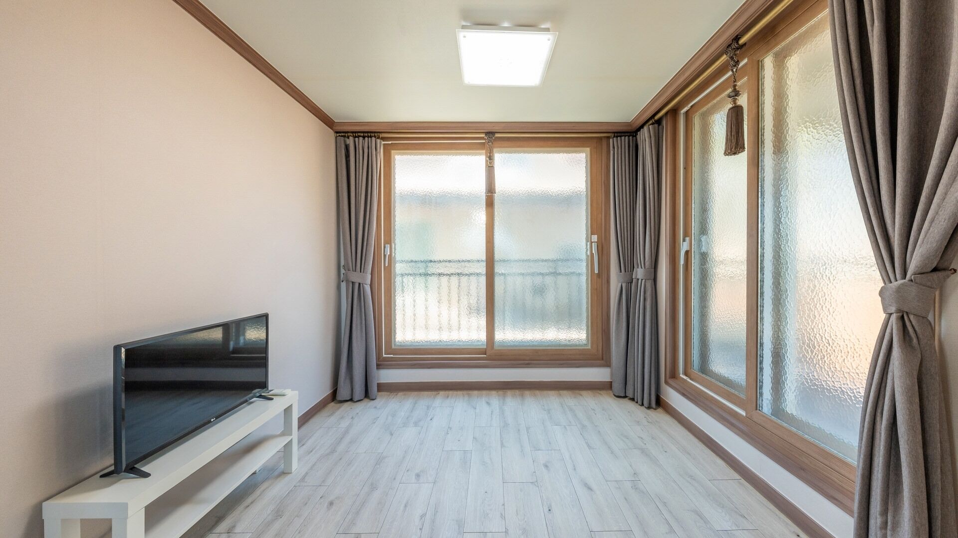 Une pièce dotée d’un téléviseur à écran plat posé sur un meuble blanc, de grandes portes coulissantes en verre dépoli et d’un parquet de couleur claire.