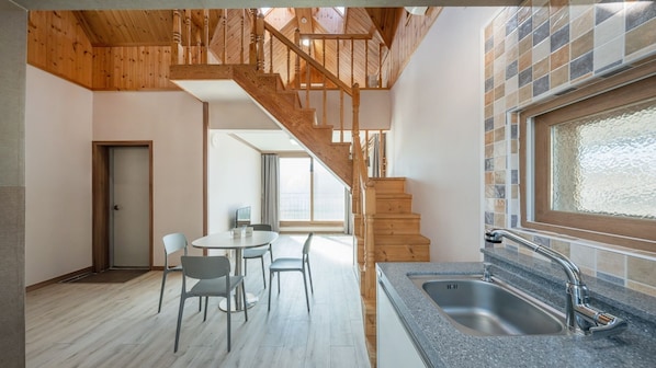 A modern kitchen with a granite countertop and stainless steel sink, a dining area with a round table and chairs, and a wooden staircase leading to an upper level.